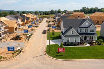 A new construction neighborhood with many houses under construction and with for sale signs in the yard along with a couple finished homes that also have for sale sign in the yard